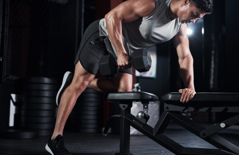 Man, weightlifting and dumbbell as bodybuilder or athlete in sports practice, training and gym. Male person, equipment and routine for challenge, muscle and wellness in workout, fitness and exercise.